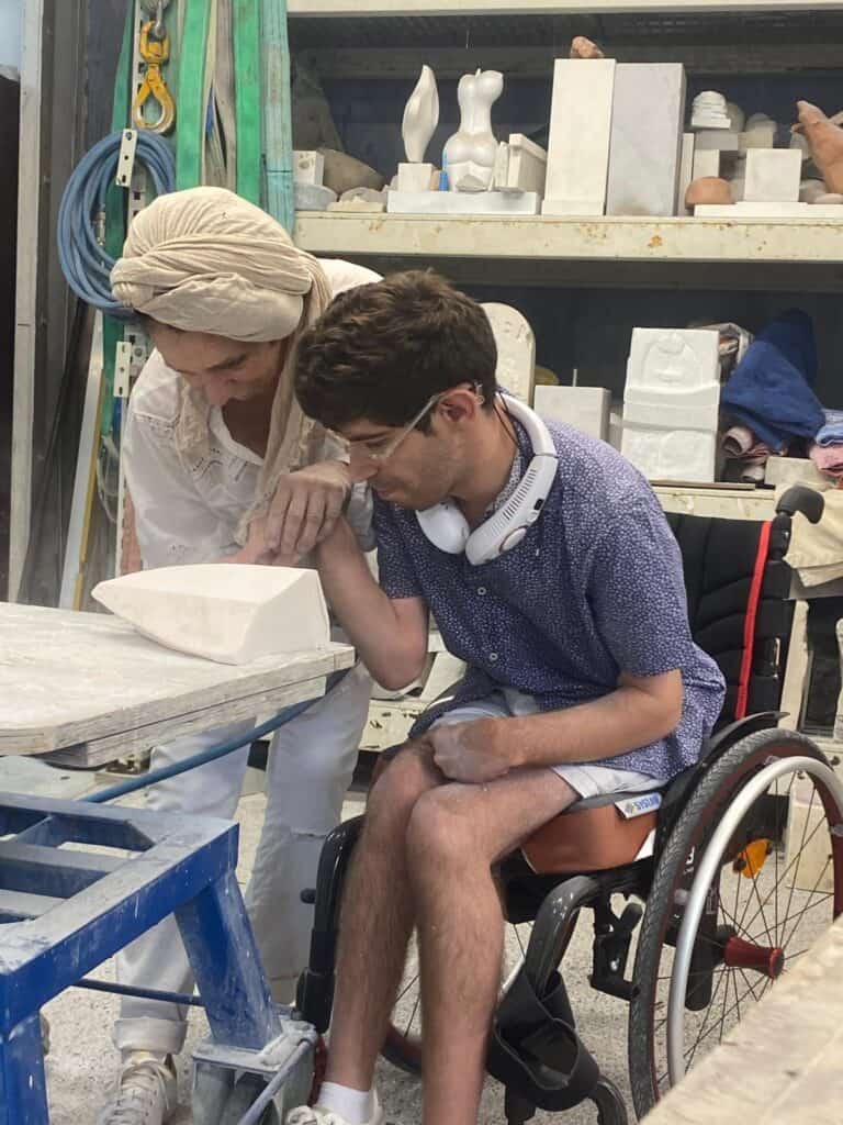 Porteur en fauteuil roulant et artisan travaillant la céramique dans un atelier artisanal.