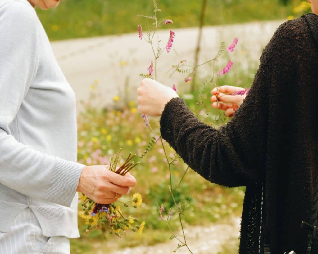 Two women gather vibrant wildflowers in a sunny Afionas field, Greece
